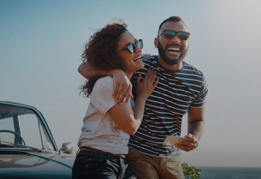 Couple laughing and hugging next to a car on the beach